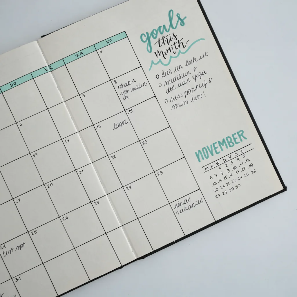 An open handwritten planner with a monthly calendar, a goals list and teal accents.